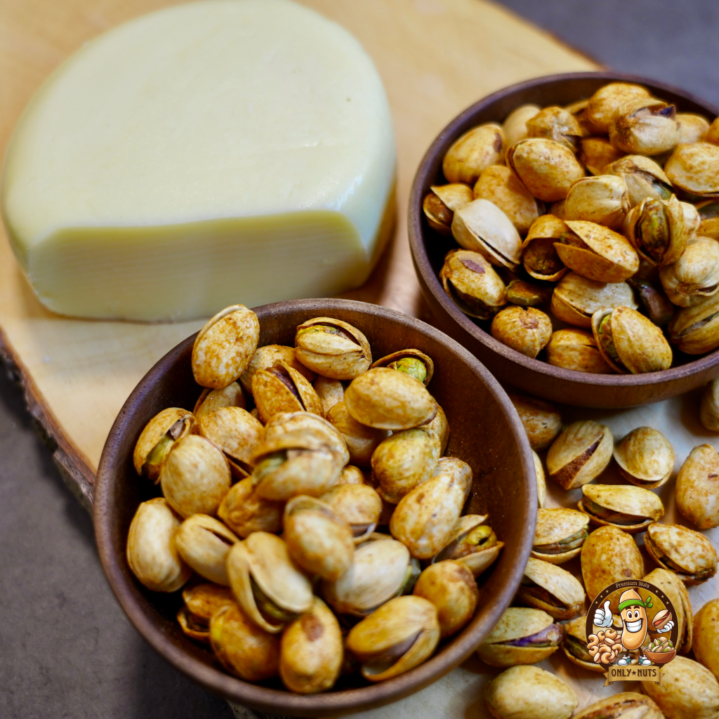 Premium Pistazien mit Käse Geschmack in rustikalen Holzschalen auf einem natürlichen Holzbrett, dekoriert mit einer aromatischen Mischung aus grobem Meersalz, Kräutern und rosa Pfefferkörnern. Perfekt für gesundes Snacking oder als Gourmet-Geschenkidee. Entdecken Sie unsere hochwertigen, nachhaltig produzierten Nüsse – ein Genuss für jeden Anlass. #Pistazien #GesundeSnacks #Nachhaltigkeit #GourmetSnacks