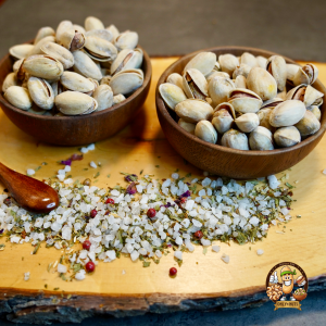 Premium Pistazien in rustikalen Holzschalen auf einem natürlichen Holzbrett, dekoriert mit einer aromatischen Mischung aus grobem Meersalz, Kräutern und rosa Pfefferkörnern. Perfekt für gesundes Snacking oder als Gourmet-Geschenkidee. Entdecken Sie unsere hochwertigen, nachhaltig produzierten Nüsse – ein Genuss für jeden Anlass. #Pistazien #GesundeSnacks #Nachhaltigkeit #GourmetSnacks